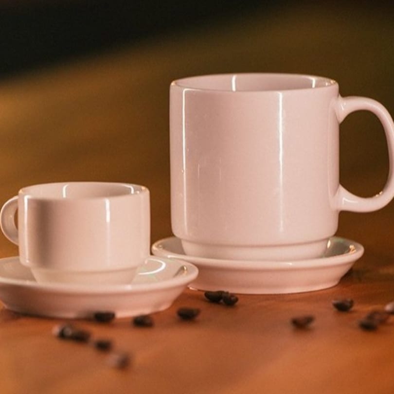 Two white coffee cups and saucers, one large and one small, with scattered coffee beans.