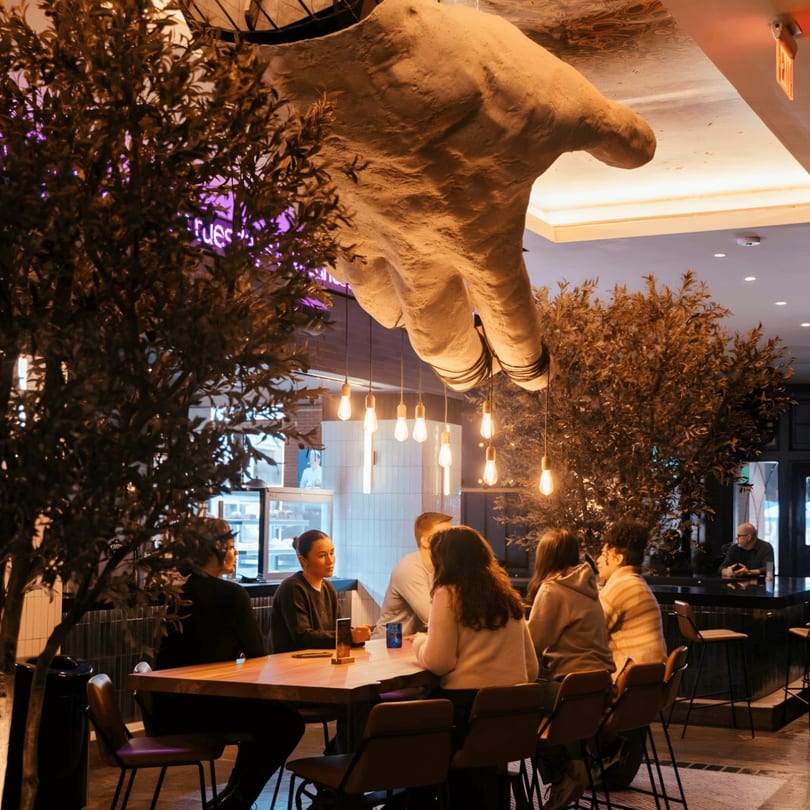 Diners seated at tables in The Operators Club, with a large hand sculpture and hanging lights overhead.