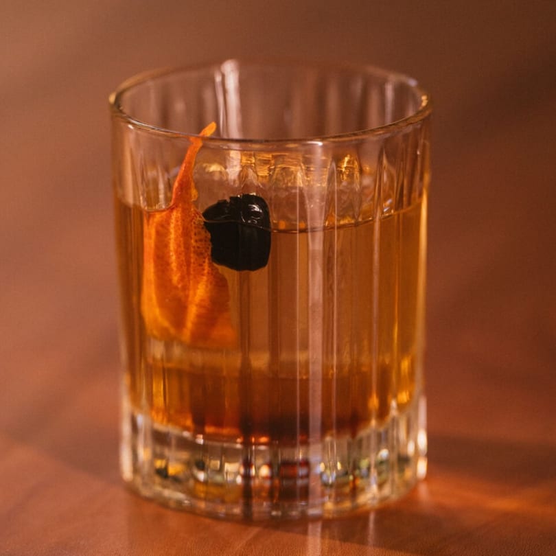 An Old Fashioned cocktail with an orange peel and cherry in a rocks glass.