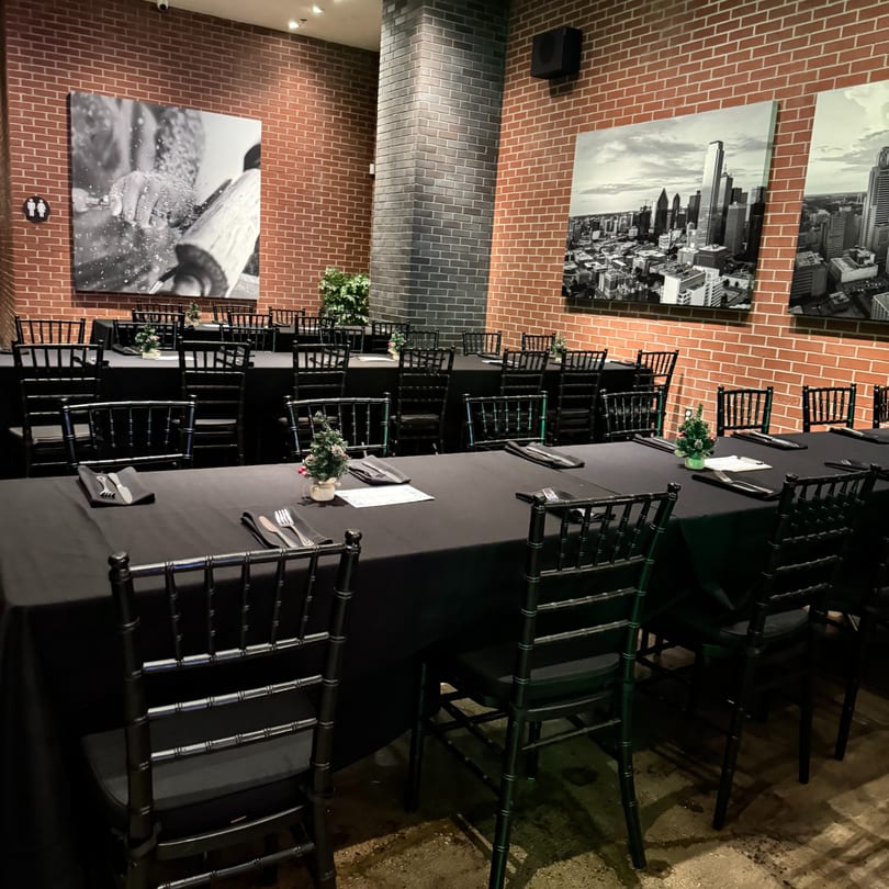 The Operators Club dining room with black tables, chairs, and brick walls adorned with cityscapes.