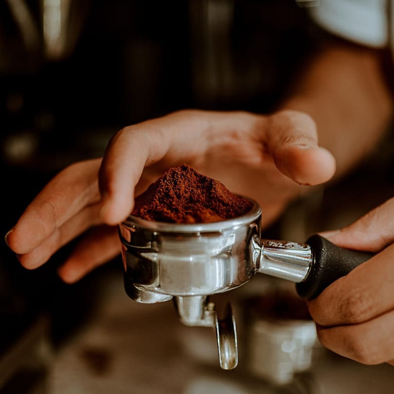 Hands holding a portafilter overflowing with finely ground coffee, ready for brewing.
