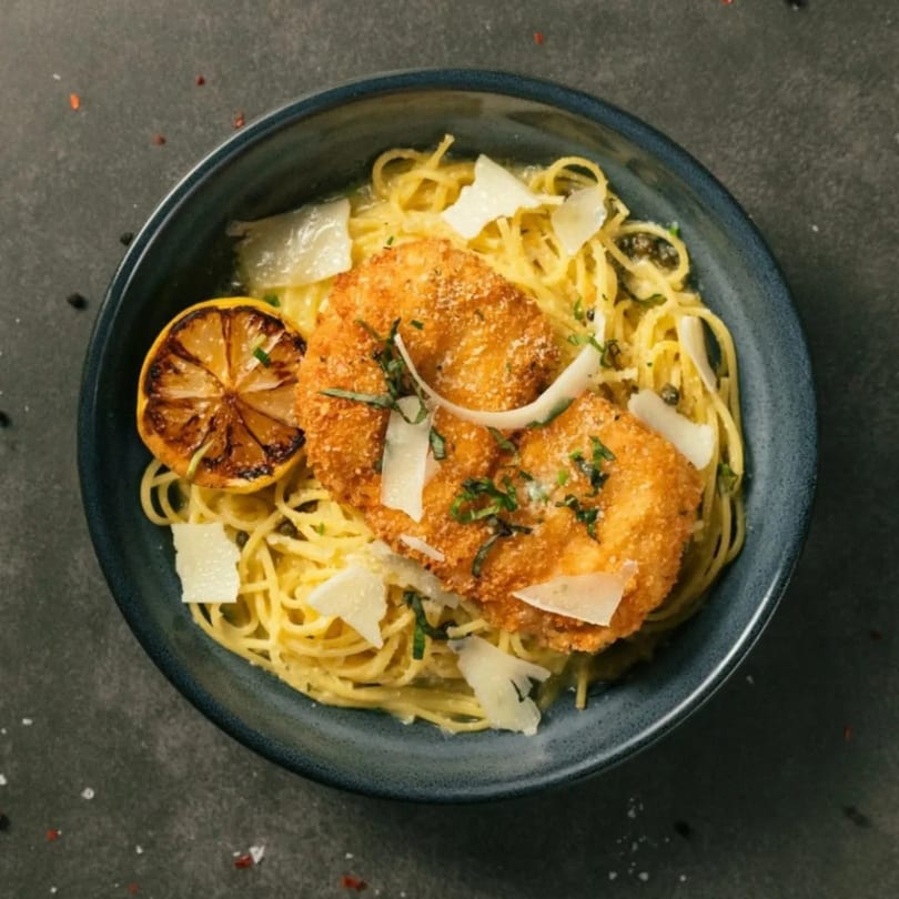 The Operators Club's chicken parmesan with spaghetti, grilled lemon, and shaved cheese in a dark bowl.
