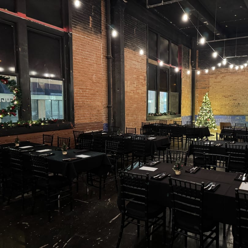 The Operators Club dining room set for a holiday event, with black tables, chairs, and a Christmas tree.